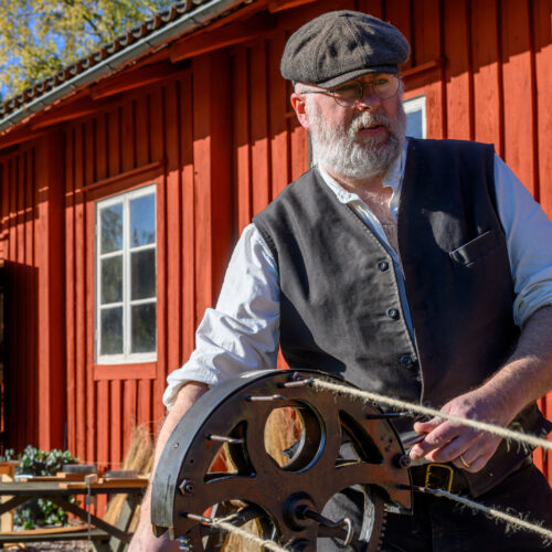 En man i keps och väst slår rep på gammalt vis.